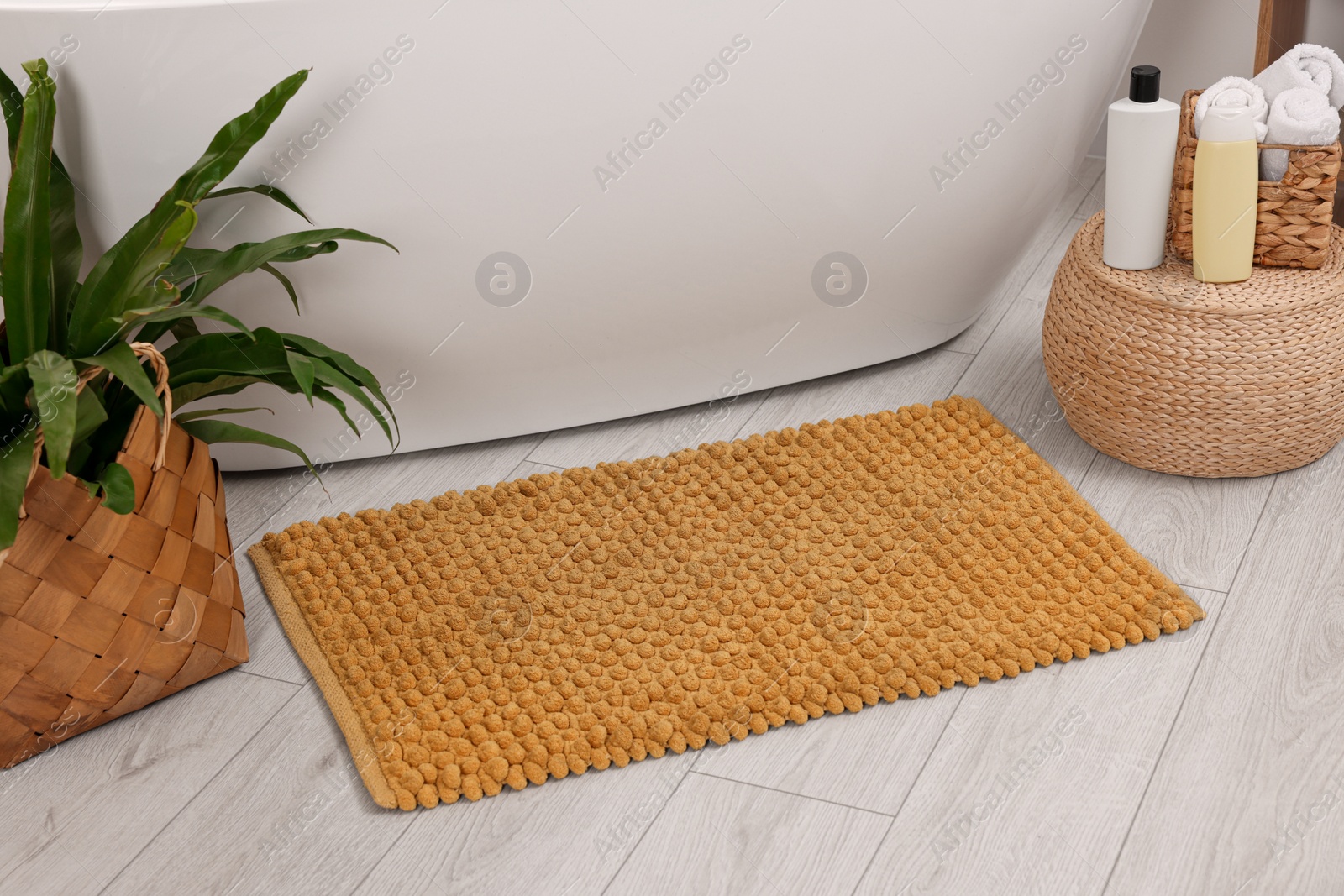 Photo of Soft bath mat, green plant and cosmetic products in bathroom