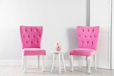 Stylish pink chairs and table near white wall in room