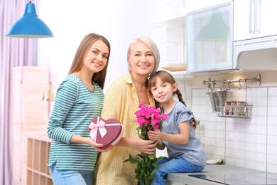 Photo of Beautiful mature lady, daughter and grandchild with gifts in kitchen. Happy Women's Day