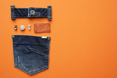 Flat lay composition with garment accessories and cutting details for jeans on orange background. Space for text