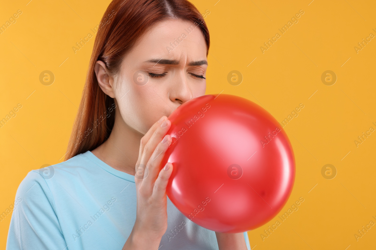 Photo of Woman inflating red balloon on orange background