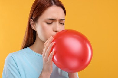 Woman inflating red balloon on orange background