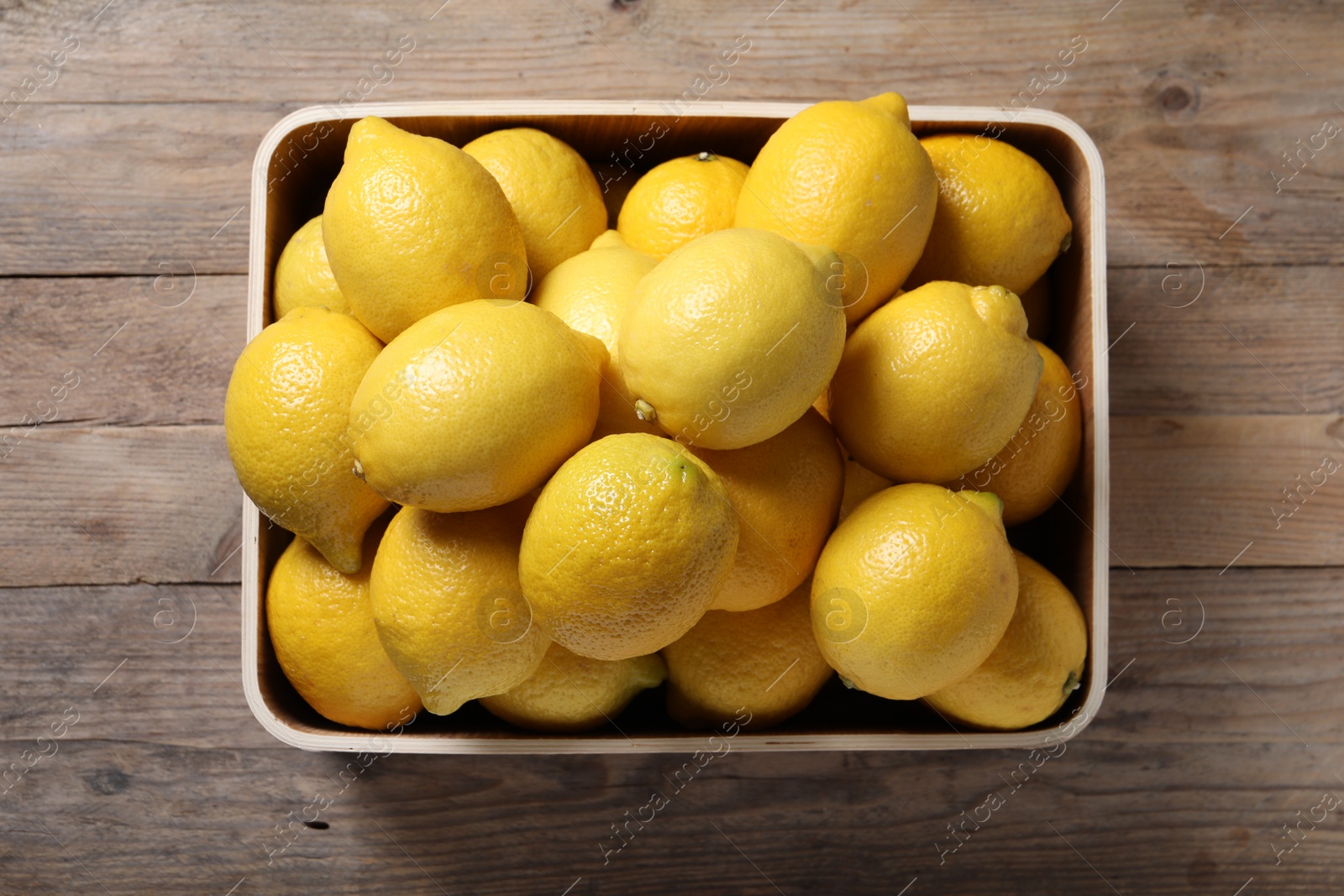 Photo of Fresh lemons in crate on wooden table, top view