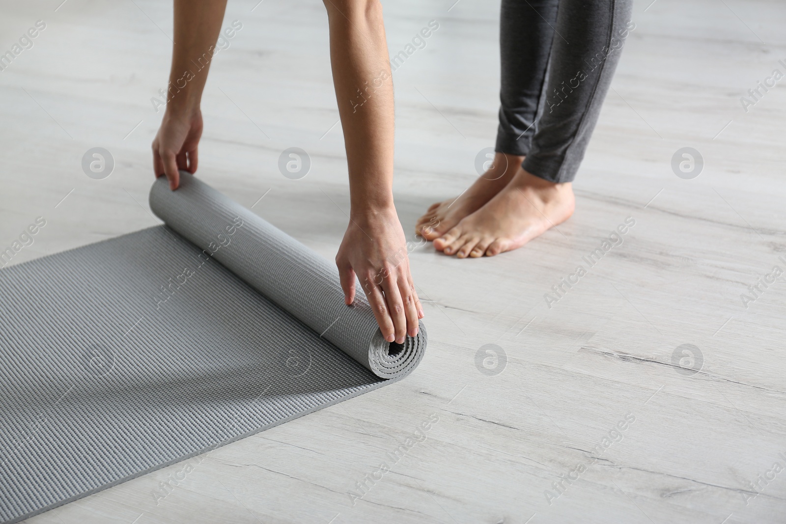 Photo of Woman rolling yoga mat on floor indoors, closeup