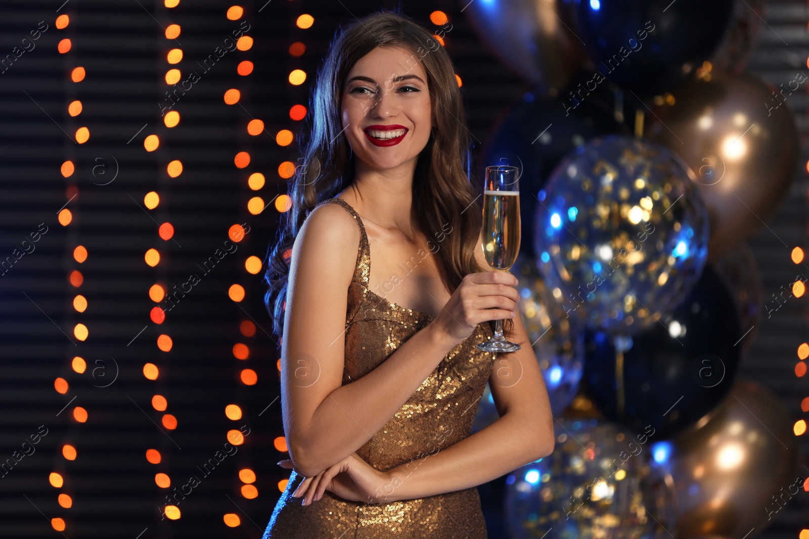Photo of Happy woman holding champagne against blurred festive lights. Christmas party