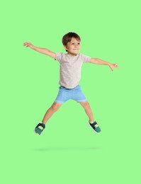 Happy boy jumping on light green background, full length portrait