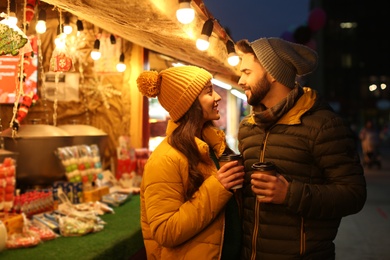 Lovely couple with cups of hot drinks spending time together at Christmas fair