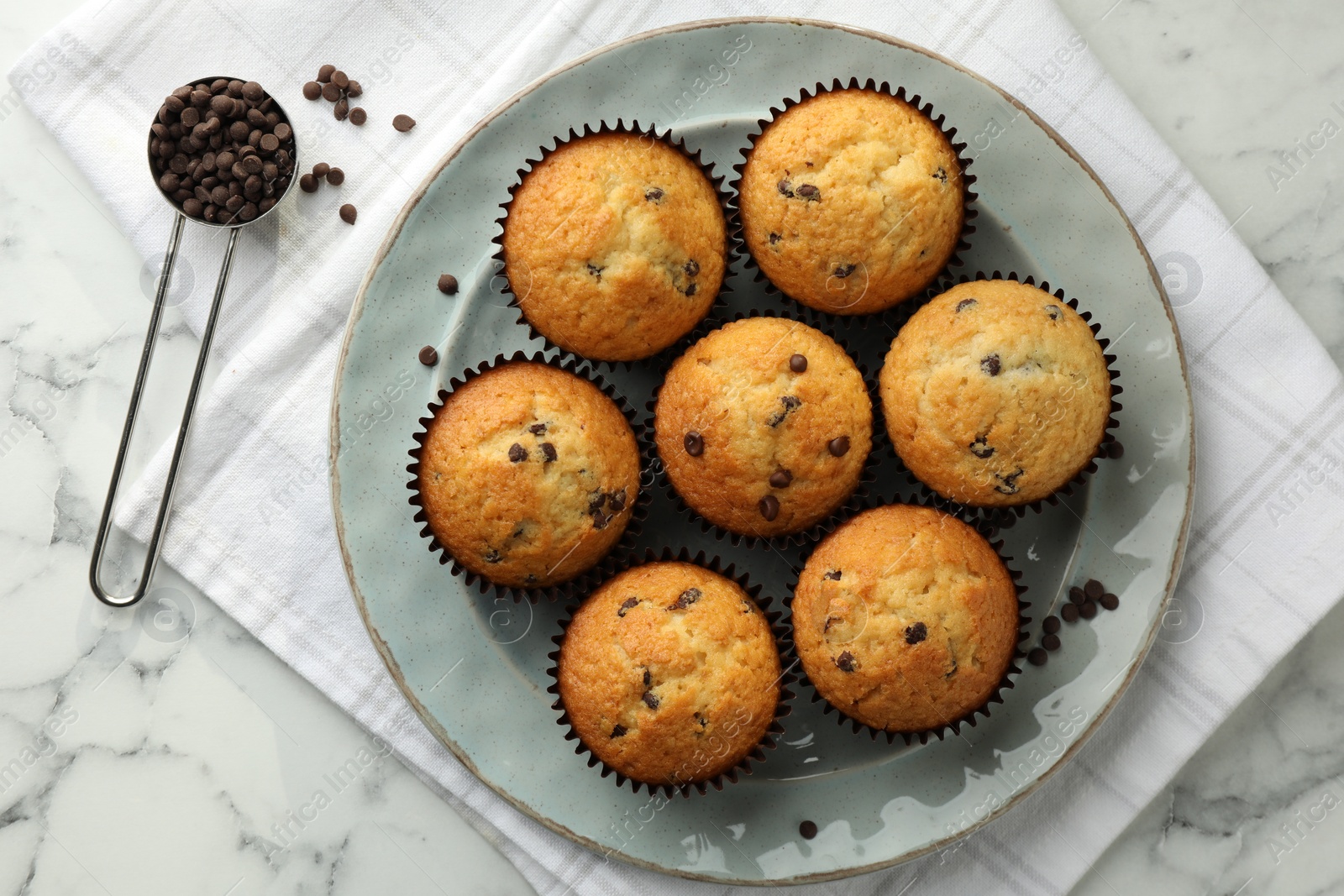 Photo of Delicious sweet muffins with chocolate chips on white marble table, top view