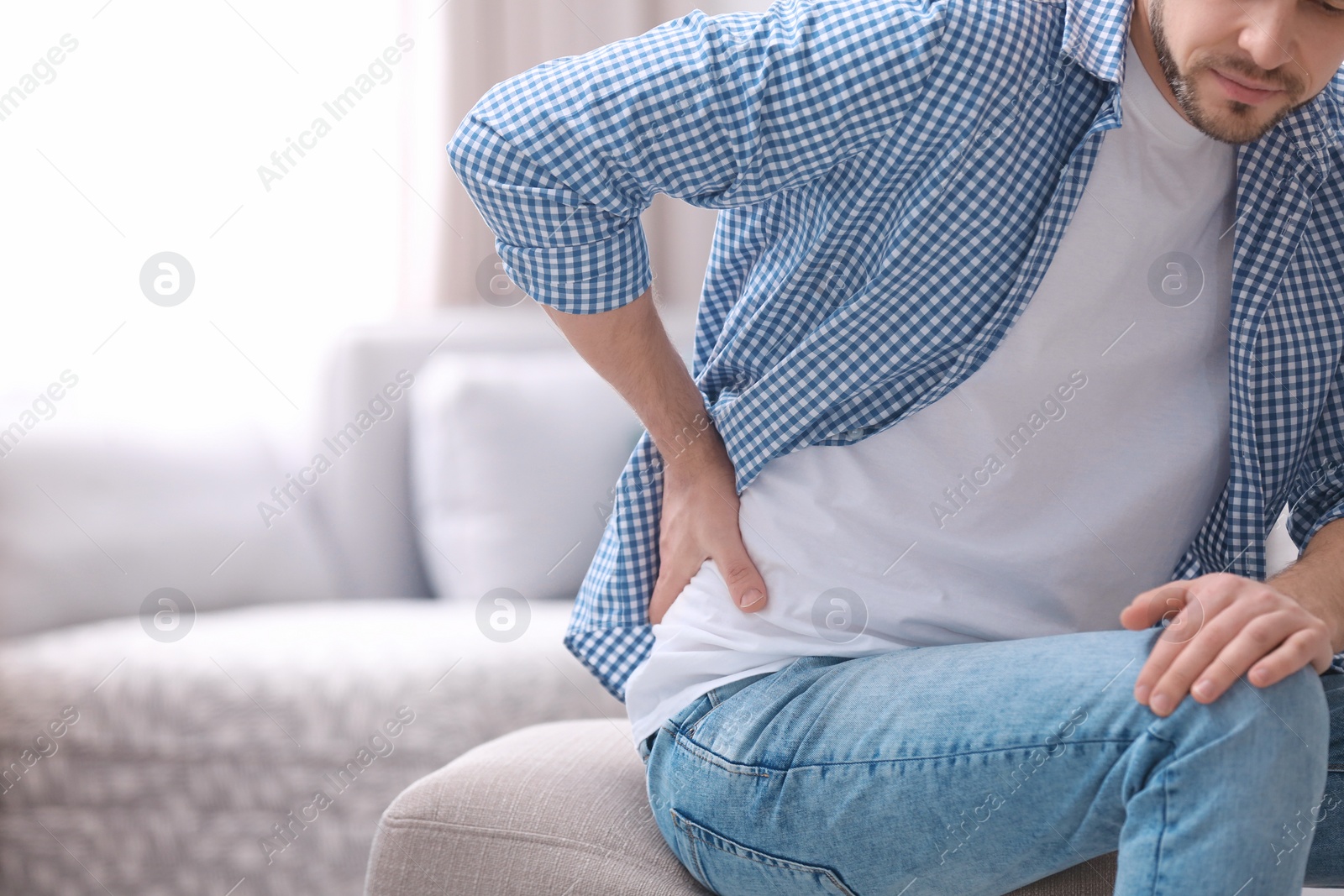 Photo of Young man suffering from back pain at home