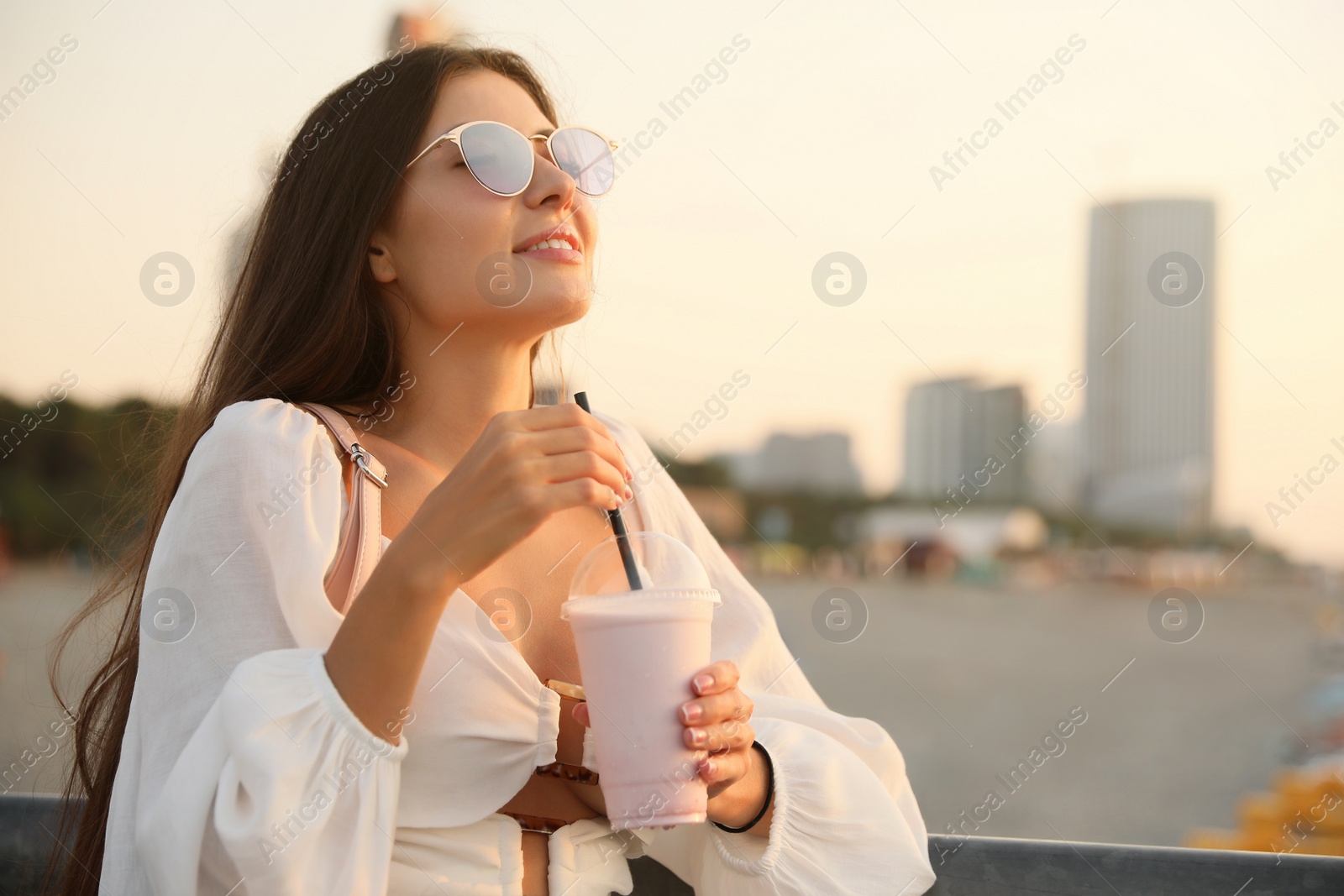 Photo of Beautiful young woman with tasty milk shake outdoors, space for text