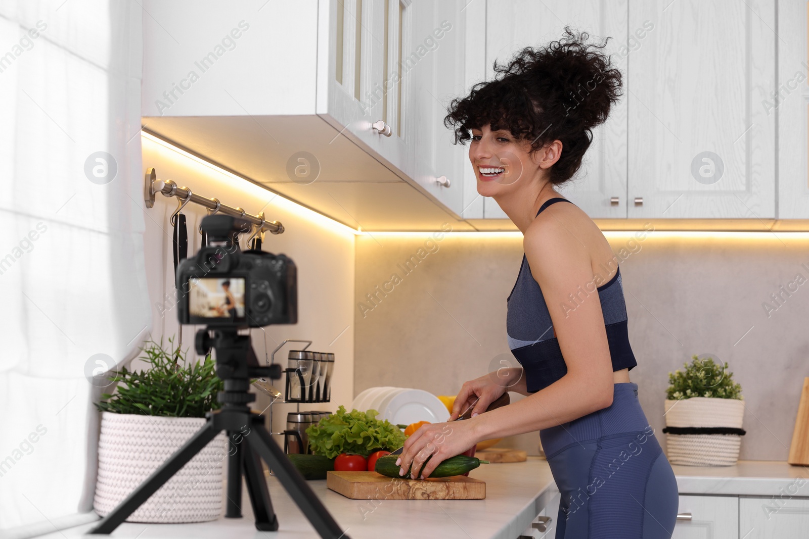 Photo of Smiling food blogger cooking while recording video in kitchen