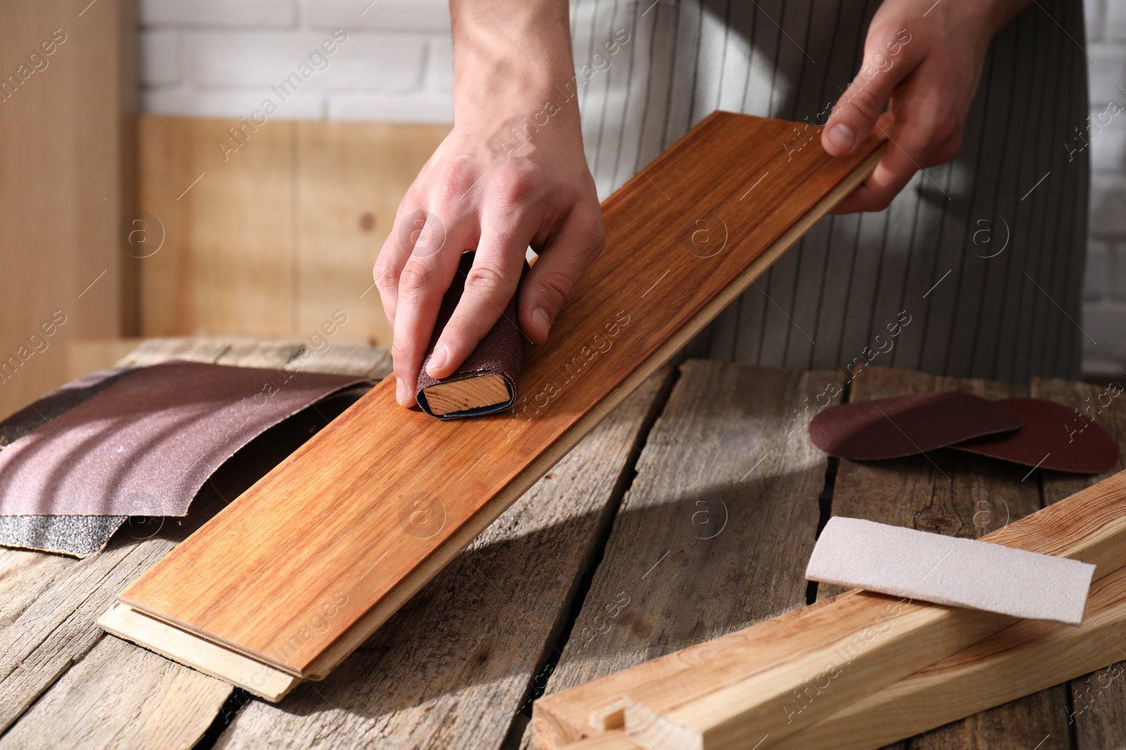 Photo of Man polishing wooden plank with sandpaper at table indoors, closeup