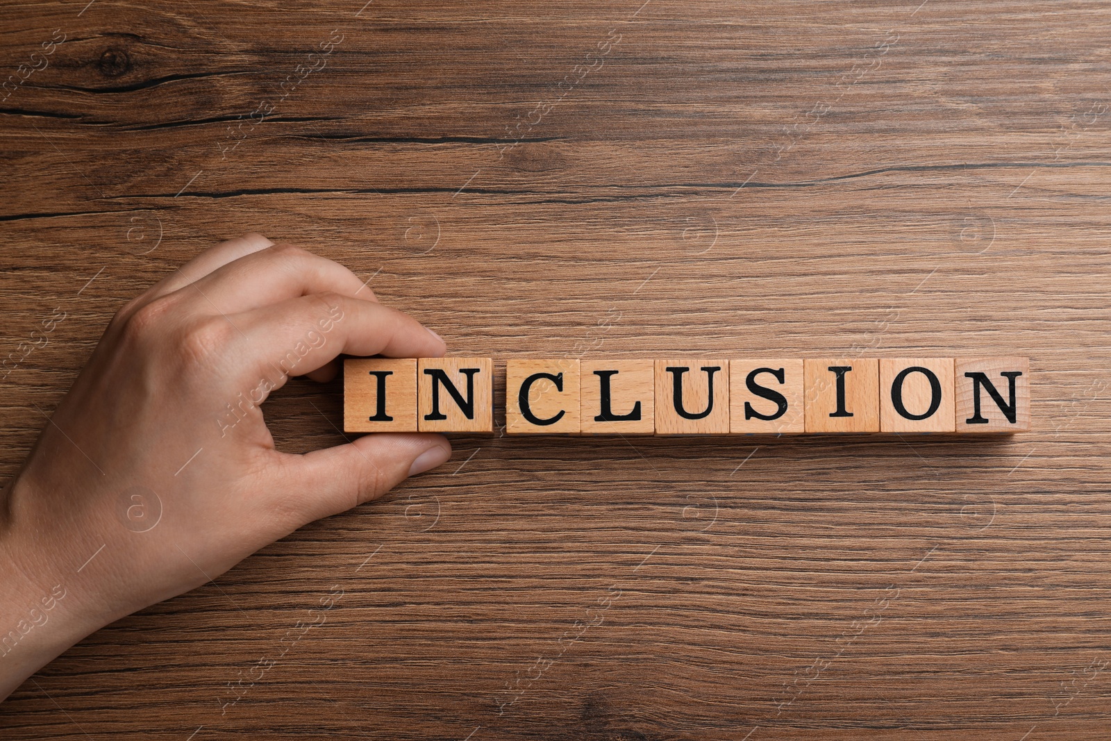 Photo of Woman making word Inclusion with cubes on wooden table, closeup with top view