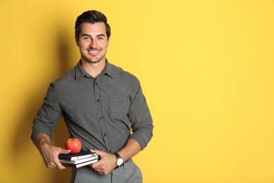 Photo of Young male teacher with books and apple on yellow background. Space for text