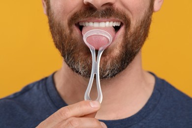 Man brushing his tongue with cleaner on yellow background, closeup