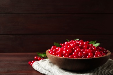 Plate with tasty ripe cranberries on brown wooden table. Space for text