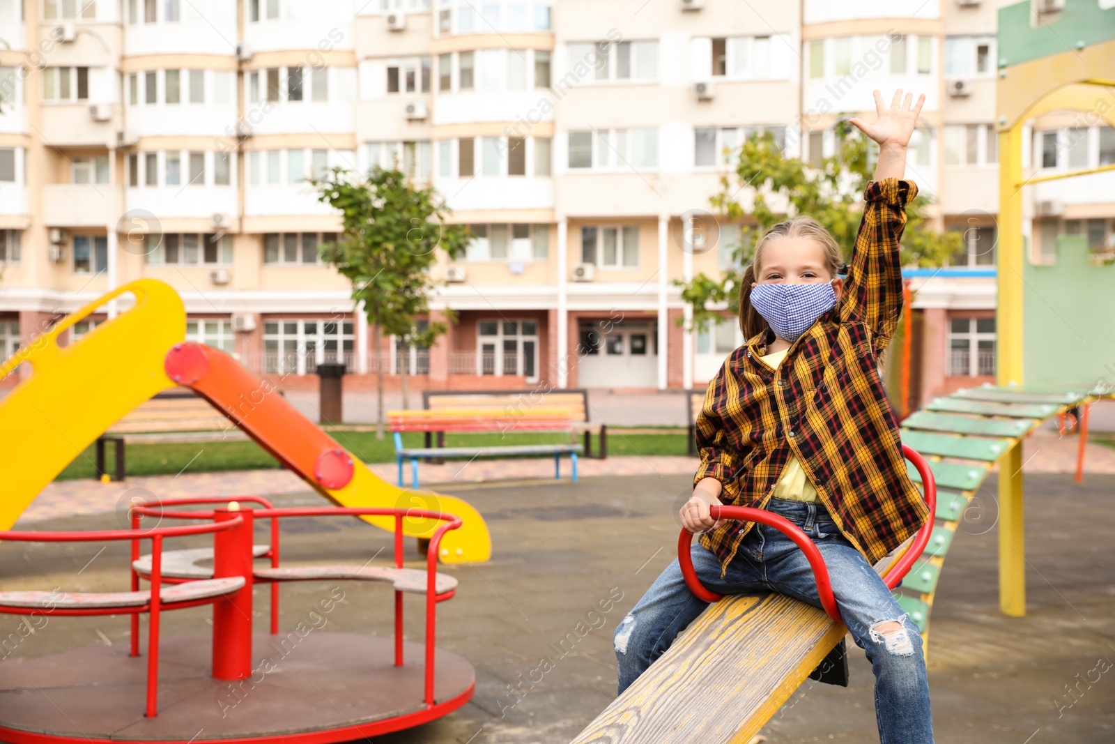 Photo of Little girl with medical face mask on playground during covid-19 quarantine