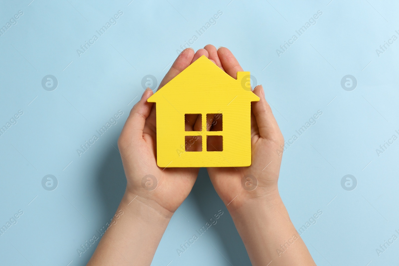 Photo of Woman holding house figure on light blue background, top view