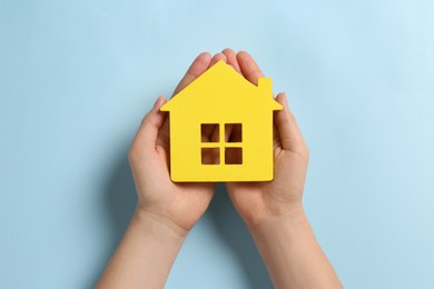 Photo of Woman holding house figure on light blue background, top view