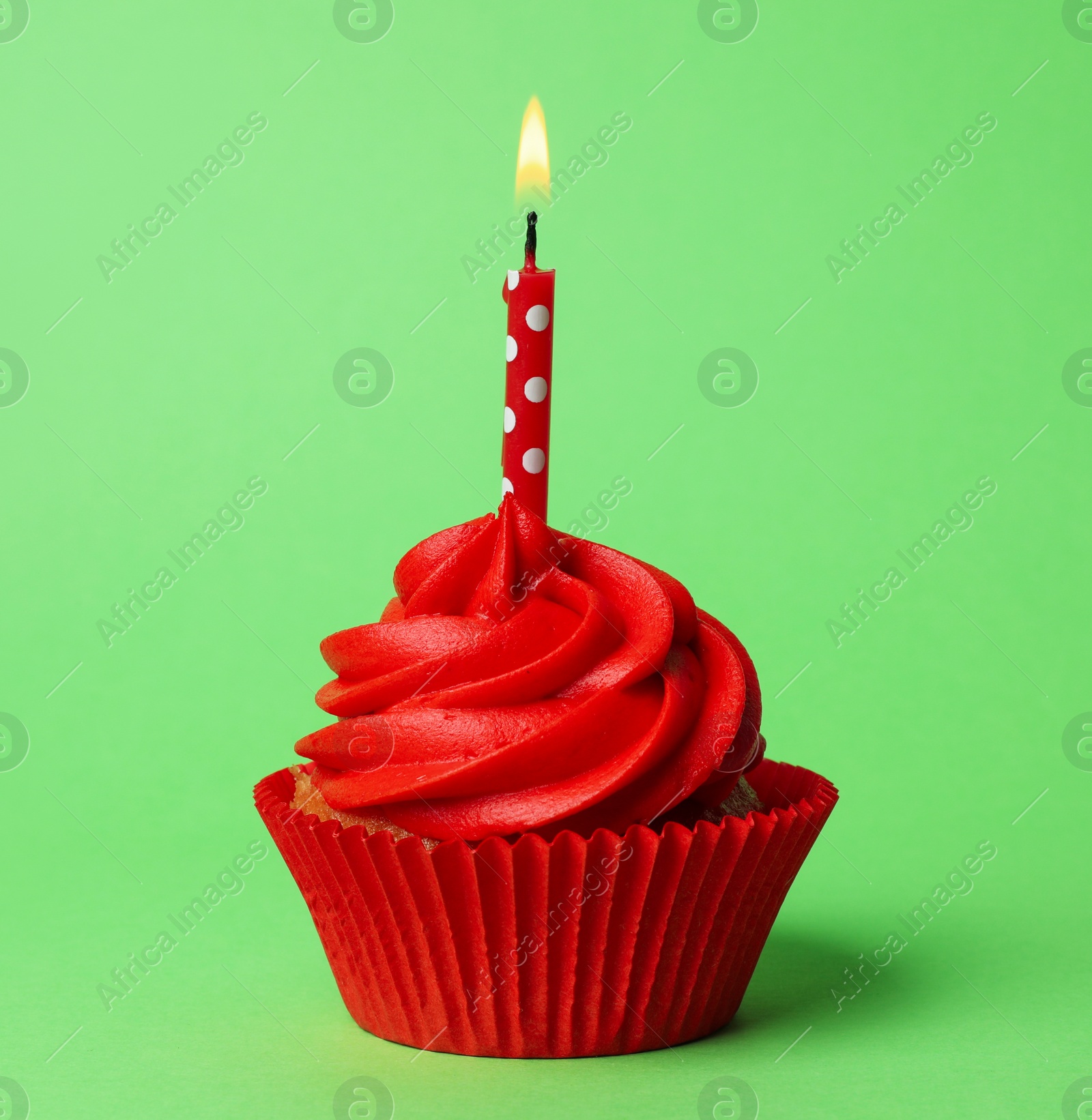 Photo of Delicious birthday cupcake with red cream and burning candle on green background