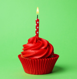 Delicious birthday cupcake with red cream and burning candle on green background