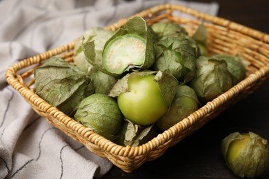 Photo of Fresh green tomatillos with husk in wicker basket on table, closeup