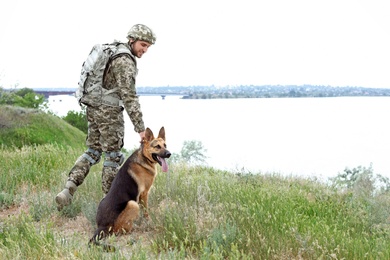 Photo of Man in military uniform with German shepherd dog outdoors