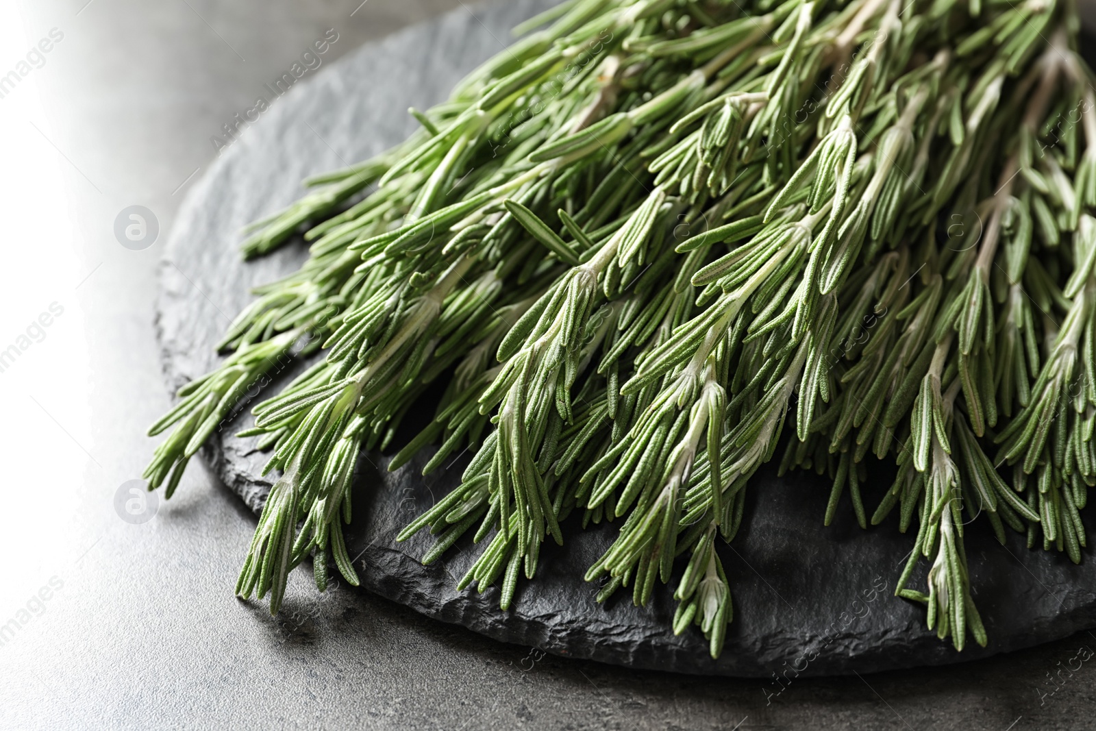 Photo of Slate plate with fresh rosemary twigs on table, closeup