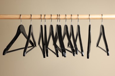Photo of Black clothes hangers on wooden rail against beige background