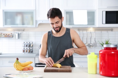 Photo of Young man preparing protein shake at table in kitchen