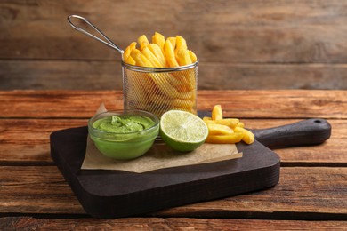 Photo of Serving board with french fries, avocado dip and lime served on wooden table