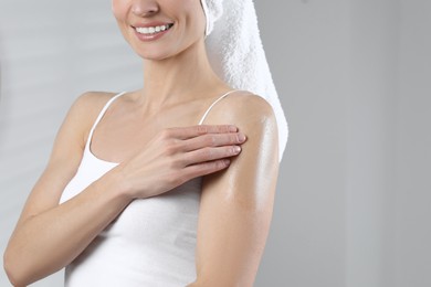 Photo of Woman applying body oil onto arm on light grey background, closeup, space for text