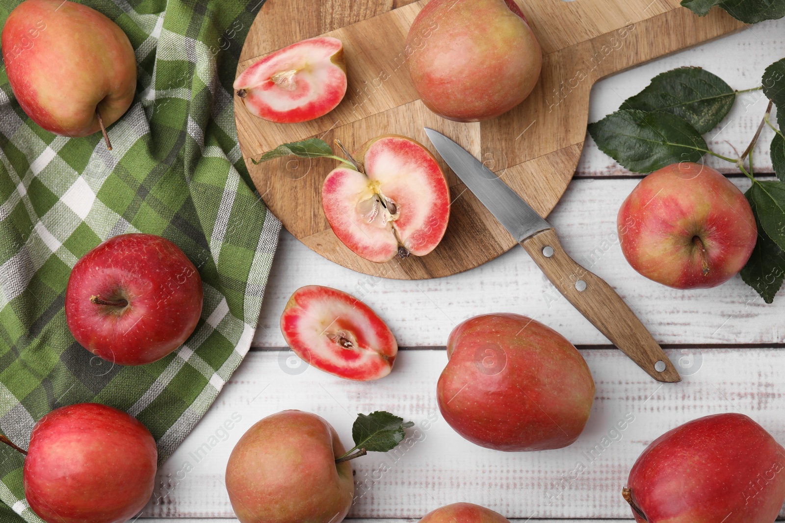 Photo of Tasty apples with red pulp and leaves on white wooden table, flat lay