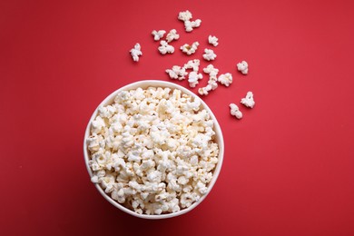 Photo of Paper bucket with delicious popcorn on red background, flat lay