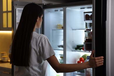 Young woman near modern refrigerator in kitchen at night