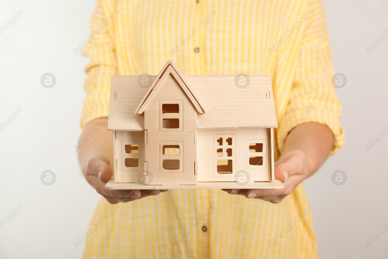 Photo of Young woman holding house model on light background, closeup