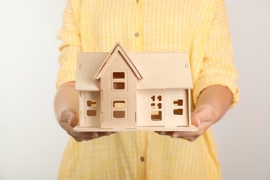 Young woman holding house model on light background, closeup