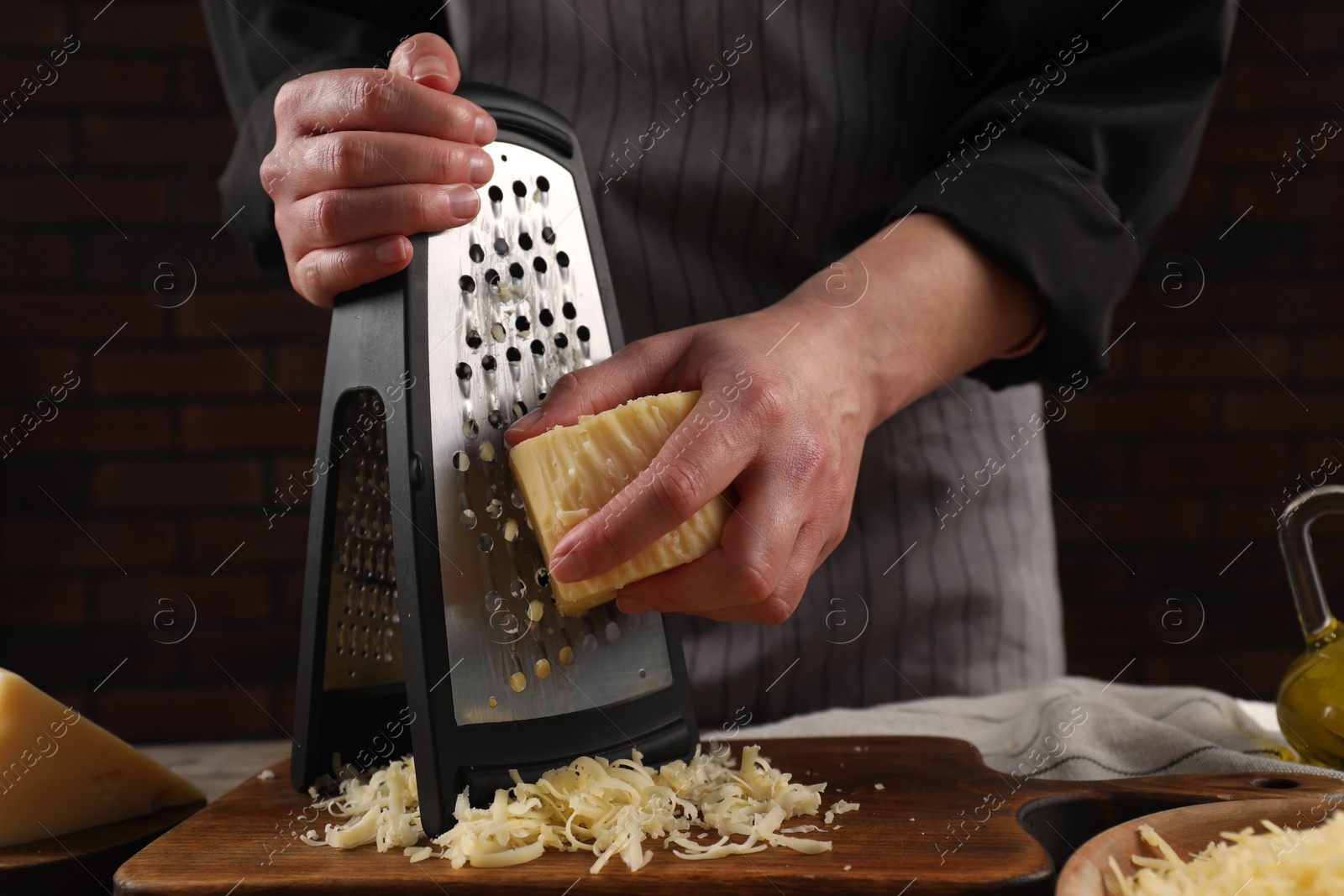 Photo of Woman grating cheese at wooden table, closeup