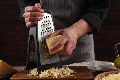 Woman grating cheese at wooden table, closeup