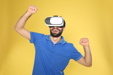 Emotional young man playing video games with virtual reality headset on color background