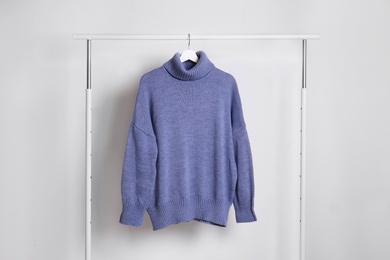 Photo of Warm sweater hanging on rack against white background