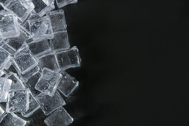 Photo of Crystal clear ice cubes with water drops on black background, flat lay. Space for text