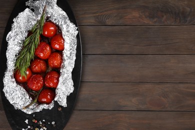 Photo of Aluminum foil with delicious baked tomatoes and rosemary on wooden table, top view. Space for text