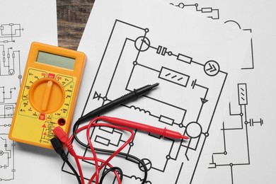 Photo of Wiring diagrams and digital multimeter on wooden table, flat lay
