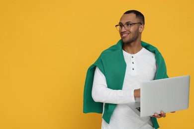 Photo of Happy young intern holding laptop on orange background. Space for text