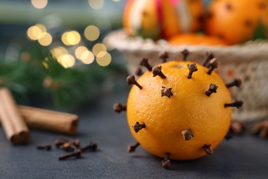 Photo of Pomander balls made of tangerines with cloves on grey table against blurred festive lights, closeup. Space for text