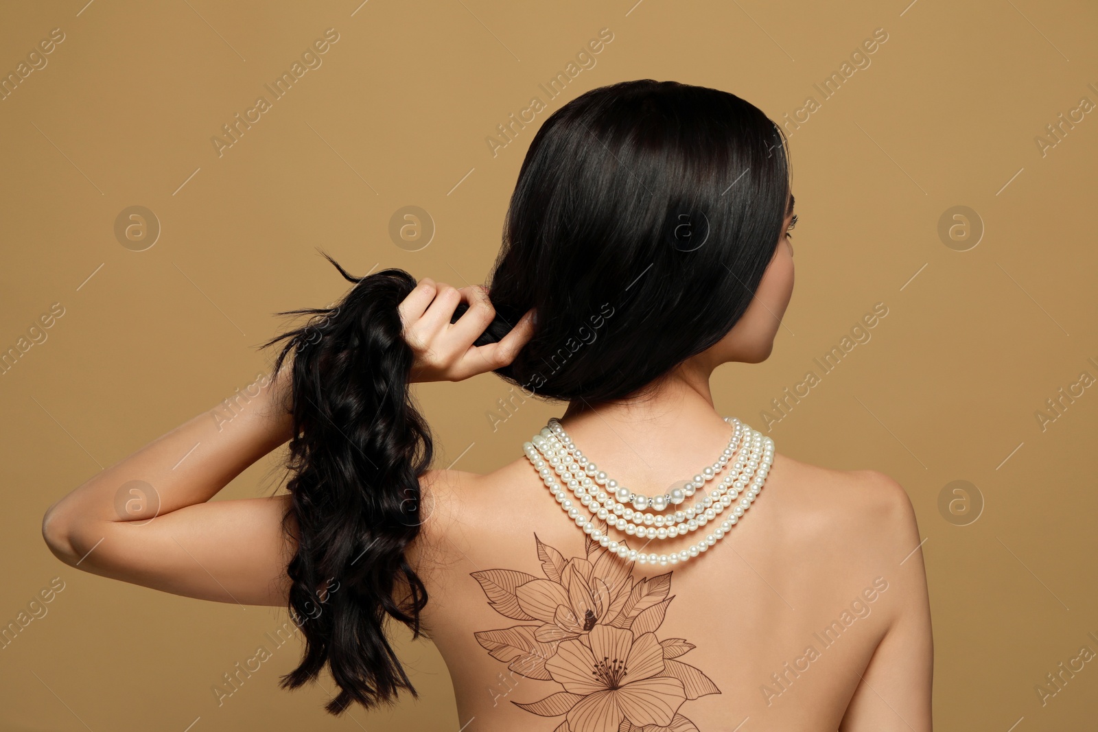 Image of Young woman with beautiful floral tattoo on brown background, back view