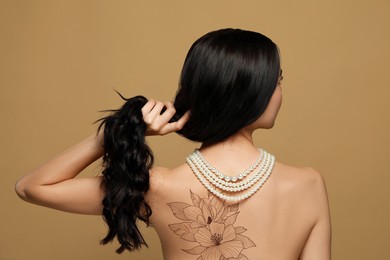 Young woman with beautiful floral tattoo on brown background, back view