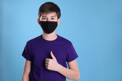 Photo of Boy wearing protective mask on light blue background, space for text. Child safety