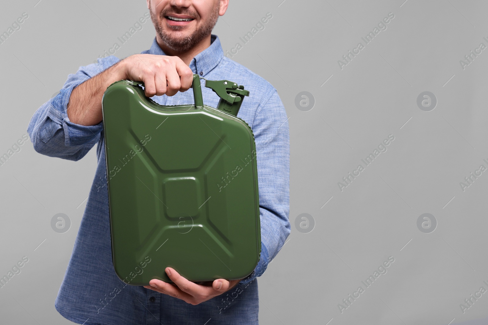 Photo of Man holding khaki metal canister on light grey background, closeup. Space for text